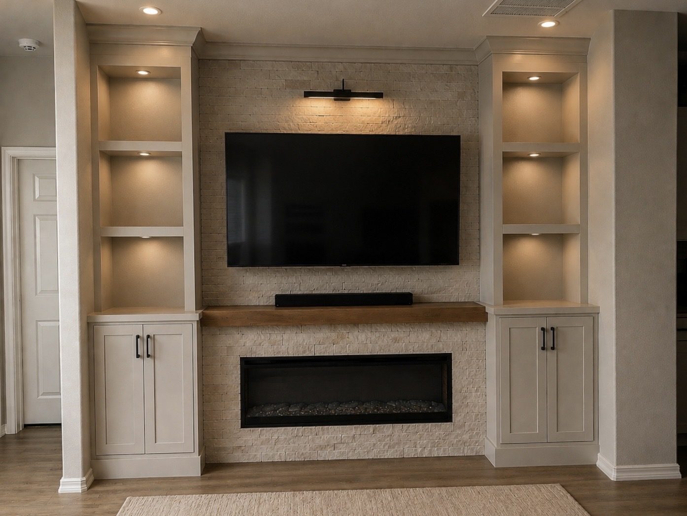 Custom great-room built-ins with lit display shelving flanking a stacked-stone fireplace wall, a white oak mantel and a linear firebox