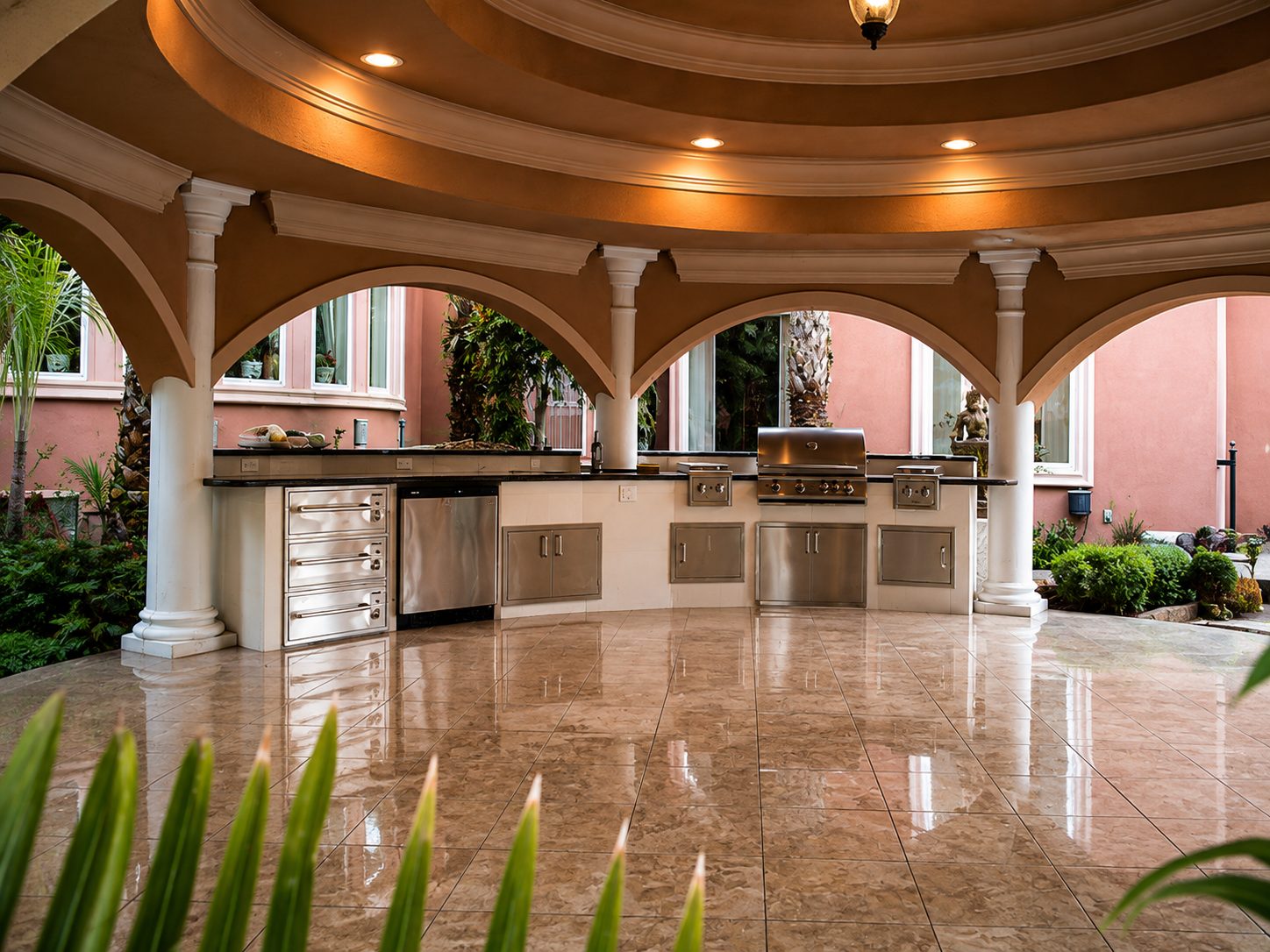 The finished gazebo: a plastered coffered dome on stone columns above a full outdoor kitchen and polished travertine floor