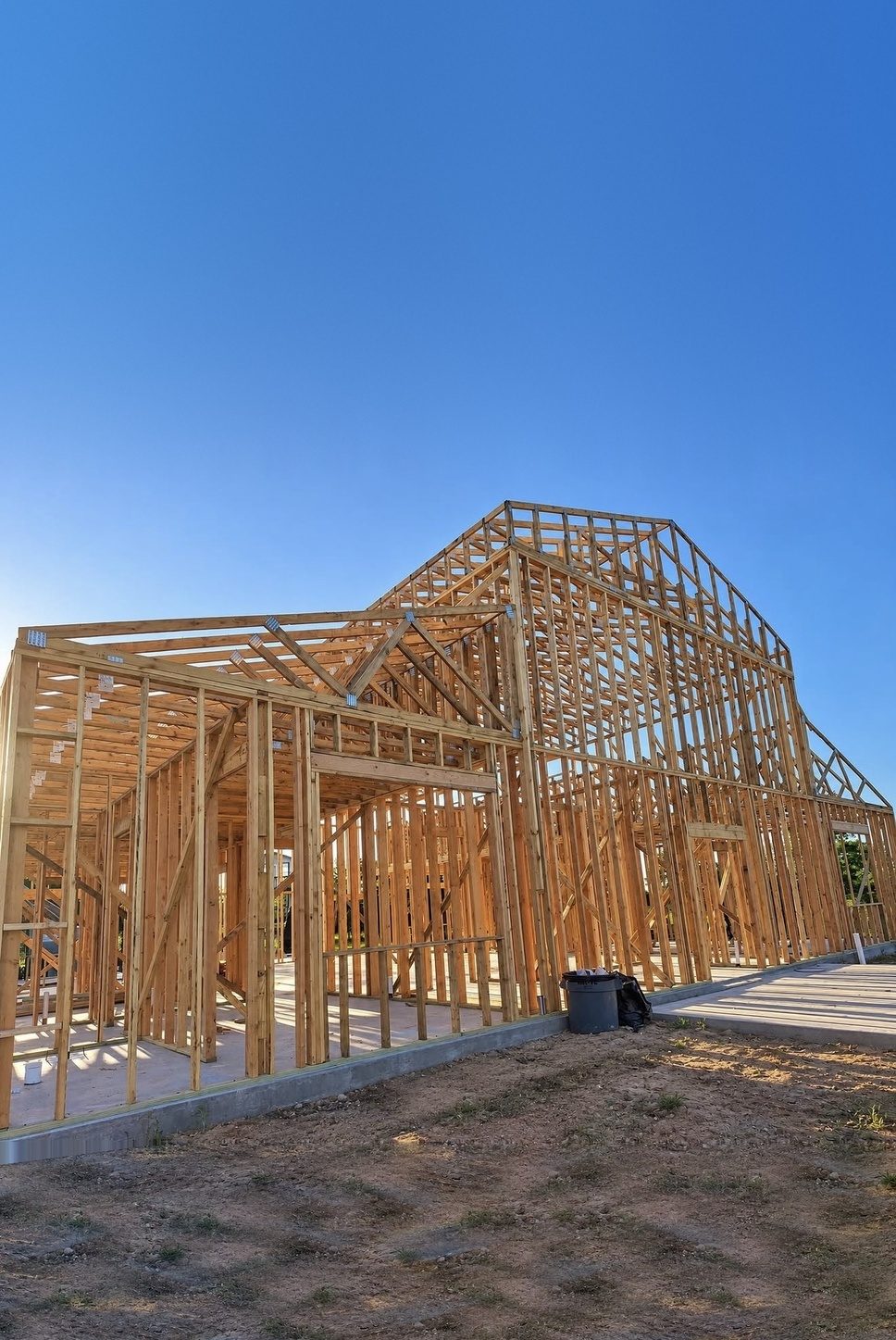 A custom home in the framing stage, its walls and roof trusses standing on a new slab